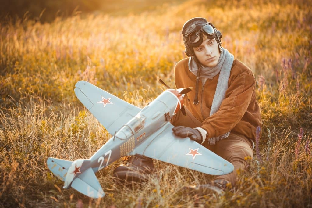 Un homme en vêtements vintage pilote un modèle d'avion en plein air.